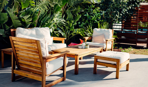 Photo of wooden patio furniture with white cushions surrounded by lush greenery