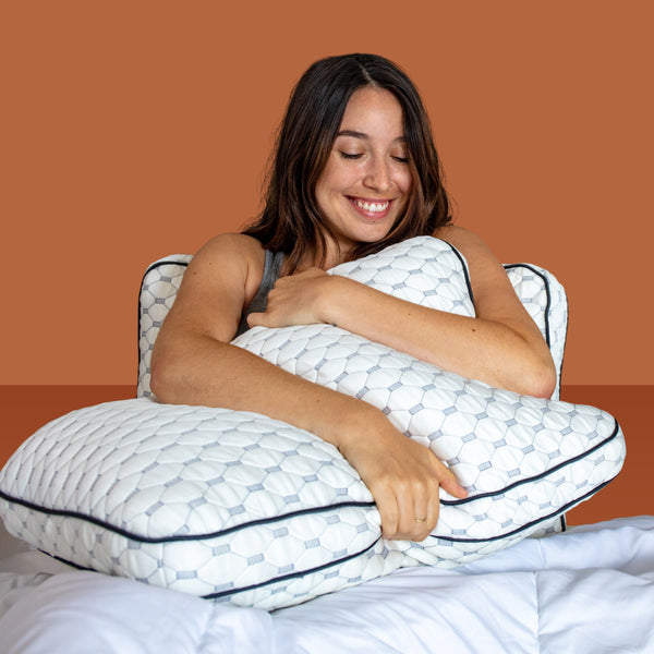 Woman smiling and hugging a pillow while leaning against another pillow (No Script)