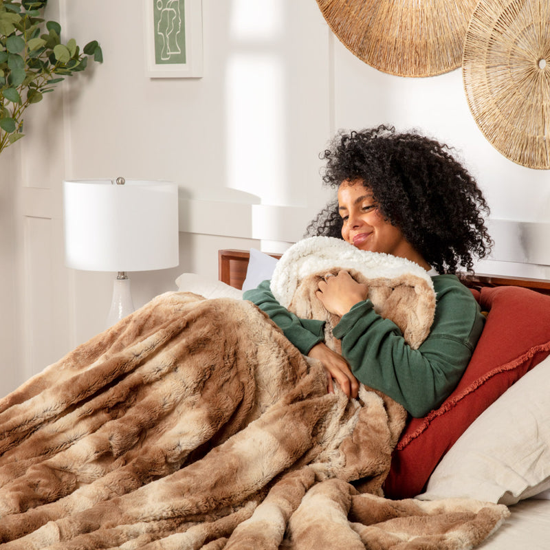 Young woman sitting in bed while wrapped up in a brown faux fur throw