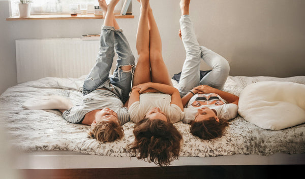 Three young women lounging and laughing on a dorm room bed.