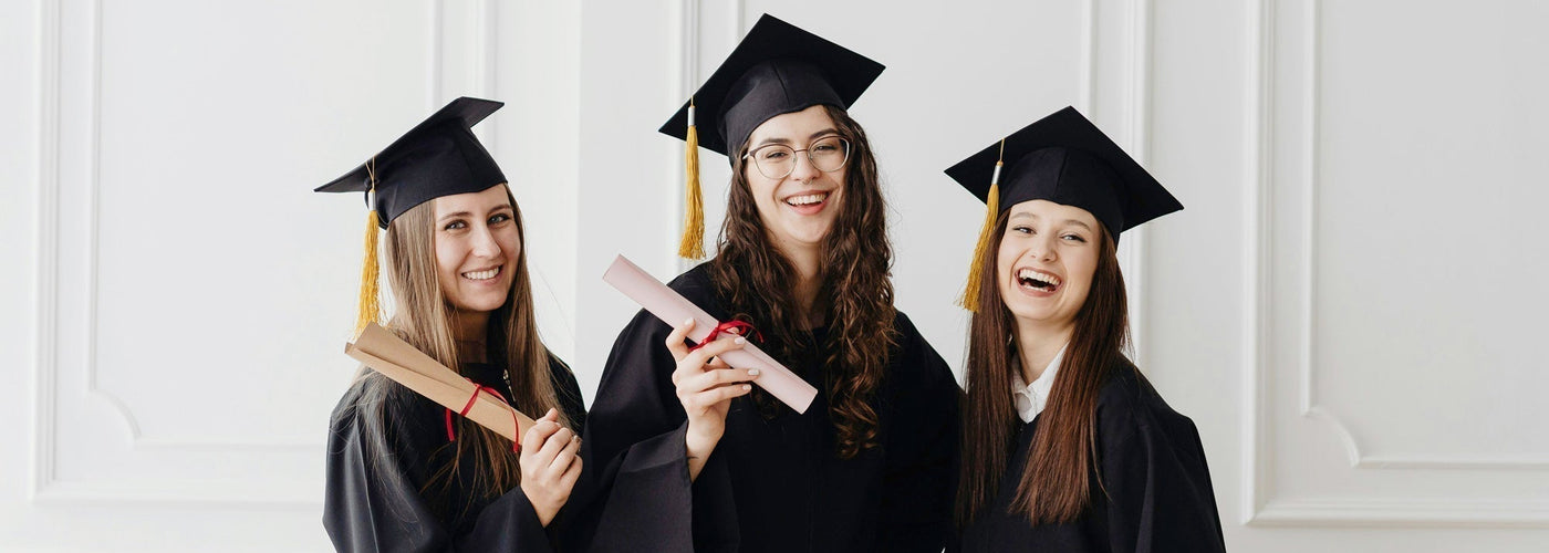 Three young women dressed in graduation caps and gowns smiling and holding up their diplomas.