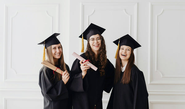 Three young women dressed in graduation caps and gowns smiling and holding up their diplomas.