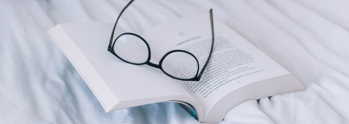 Artistic image of eyeglasses and a book alone on a bed 