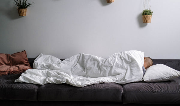 Photo of a person wrapped in a comforter while sleeping on a sofa