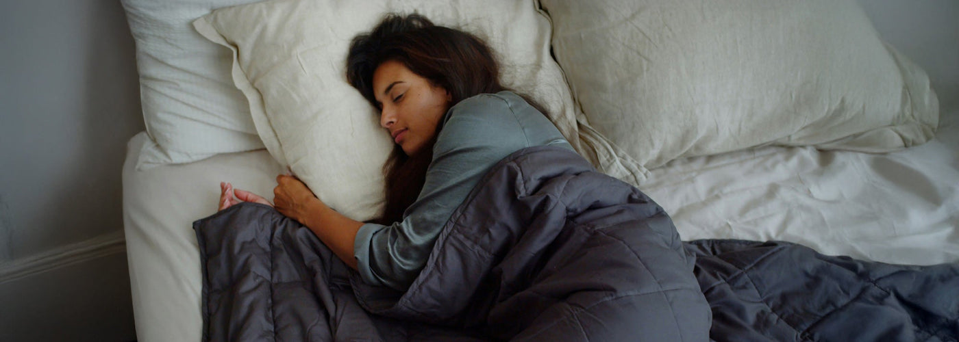 A woman with dark hair sleeping in her bed with a dark blue comforter