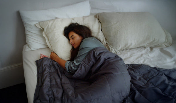 A woman with dark hair sleeping in her bed with a dark blue comforter