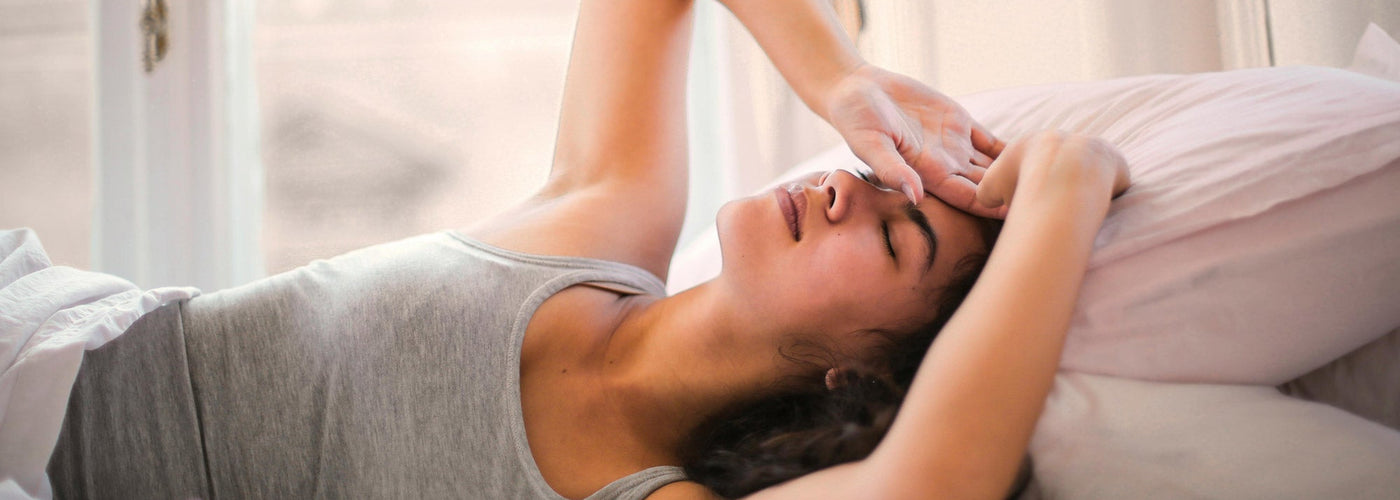 Woman laying in be with her arms up over her face like she is stressed and cannot sleep