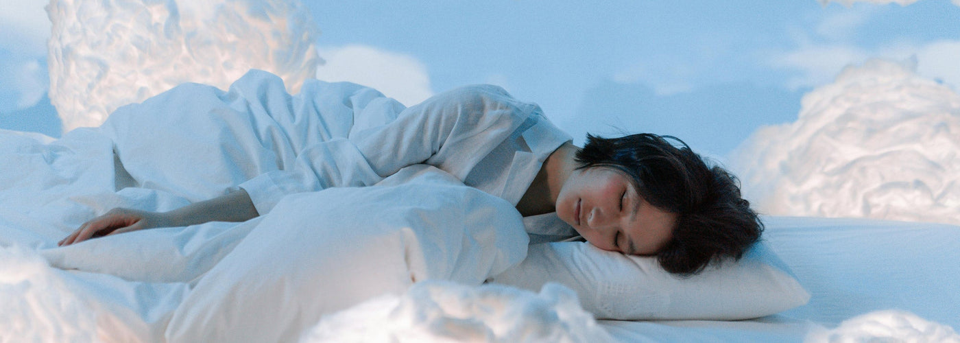 A woman laying down with a pillow and comforter in a blue room surrounded by white fluffy clouds