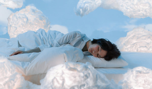 A woman laying down with a pillow and comforter in a blue room surrounded by white fluffy clouds