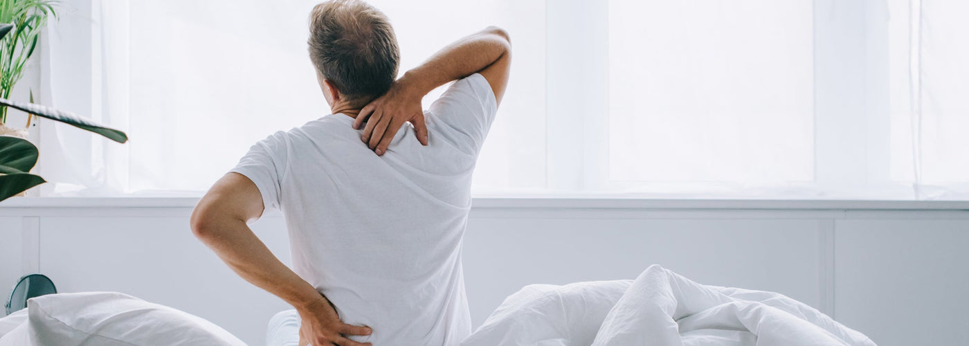 Man holding back and neck like he's in pain while sitting in bed