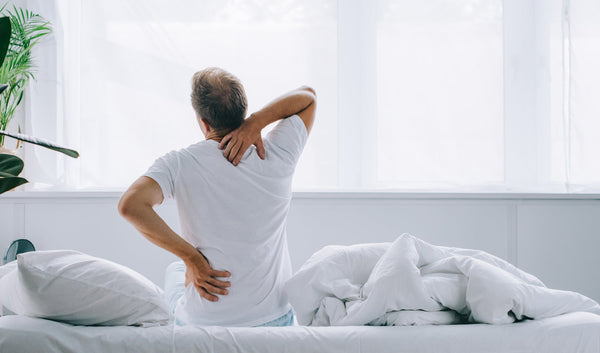 Man holding back and neck like he's in pain while sitting in bed
