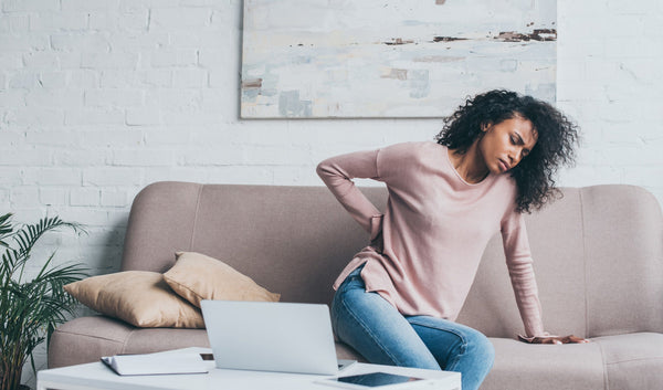 Woman leaning over while sitting on a couch and holding her back like she's in pain