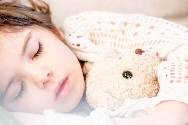 Small child in whit sweater sleeping with her teddy bear