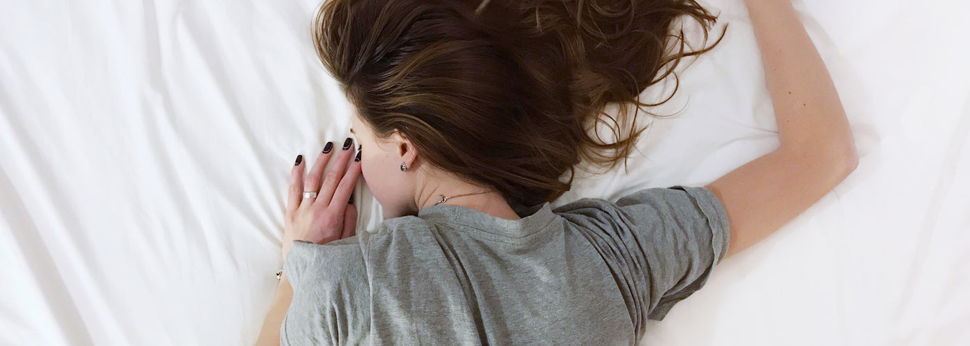 Overhead view of a woman in a t-shirt lying face down on her bed