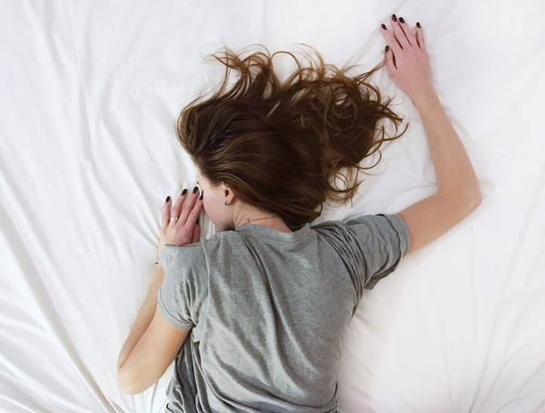 Overhead view of a woman in a t-shirt lying face down on her bed