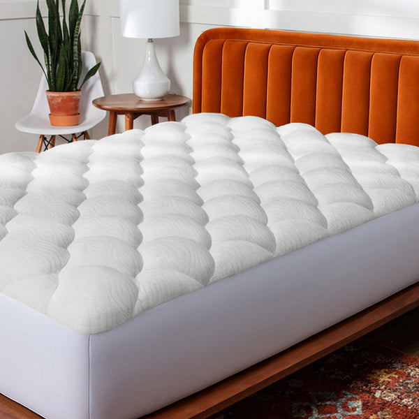 White mattress topper on a bed with an orange headboard in a bedroom setting. (No Script)