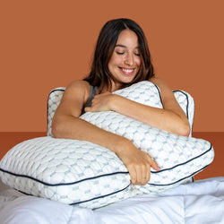Woman smiling and hugging a pillow while leaning against another pillow