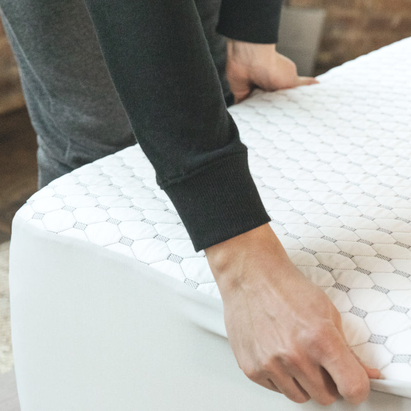 A person fitting a white and gray mattress protector onto a mattress.