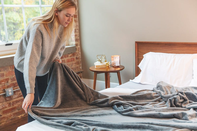 Woman laying gray fleece blanket out on bed.