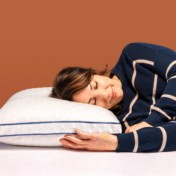 Woman resting her head on a white pillow with dark blue piping on the edge. (No Script)