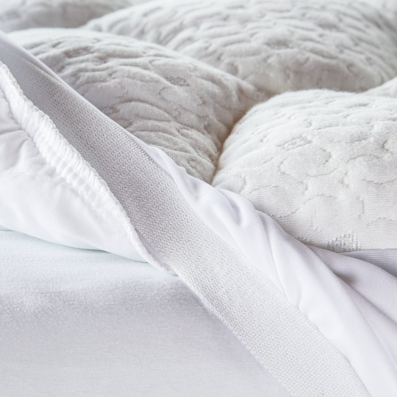 Close up view of a white pillow top mattress pad with the elastic band pulled up so you can see it.