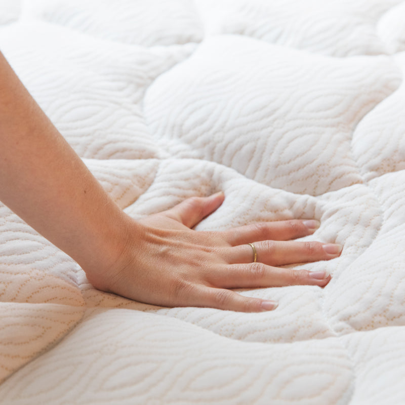 Photo of a person pressing their hand onto a white pillow top mattress pad with copper stitching.