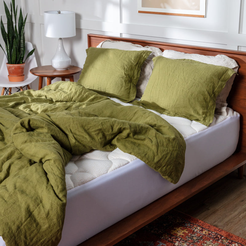 A bed fitted with a white pillow top mattress pad with copper stitching with green bedding on top of it.